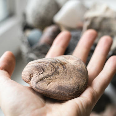 Eine Hand hält einen runden, marmorierten Stein mit natürlichen Mustern.